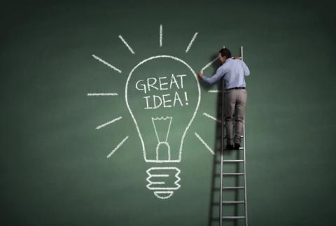 Man on ladder drawing light bulb on big blackboard